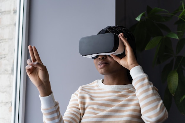 African woman wearing VR helmet touching air with finger testing modern hitech future gadget