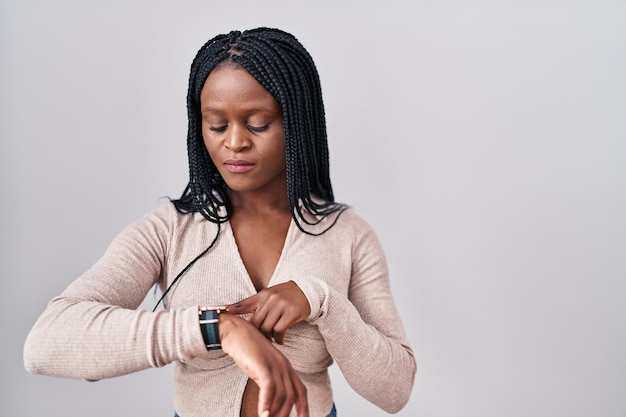 흰색 배경 위에 머리를 땋고 손목 시계로 시간을 확인하는 아프리카 여성, 편안하고 자신감