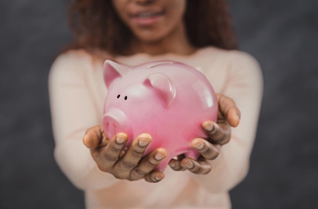 African woman with her savings in a piggy bank on grey background, selective focus