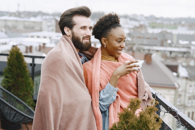 African woman with husband. Guy and girl in a plaid. Lovers drinking coffee on balcony.