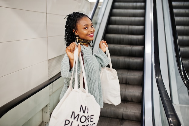 African woman with shopping eco bags on escalator at mall.