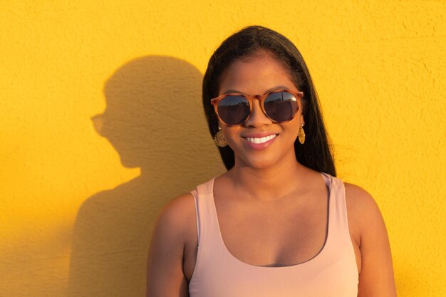 黄色の背景で笑顔のサングラスとアフリカの女性