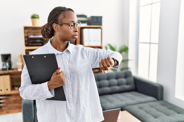 African woman working at psychology clinic checking the time on wrist watch relaxed and confident