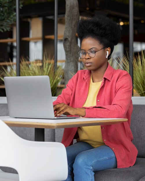 Donna africana giovane e bella con una camicia rosa in una stanza di coworking che lavora su un laptop