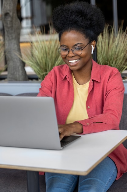 Donna africana giovane e bella con una camicia rosa in una stanza di coworking che lavora su un laptop