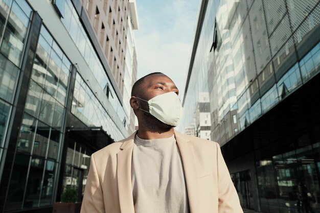 African young businessman in protective mask standing in the city with modern buildings in the background