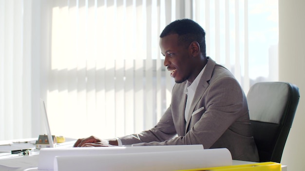 Photo african young businessman using laptop sitting in modern white office