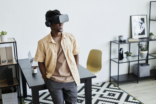 African young businessman in virtual reality glasses working online while standing at office