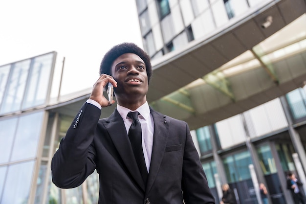아프리카 의 젊은 사업가 가 금융 건물 밖 에서 전화 를 사용 하고 있다