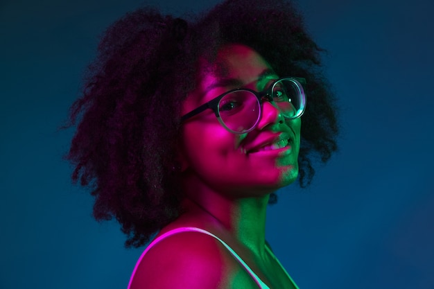 African young girl's portrait on dark blue studio background in pink neon light.