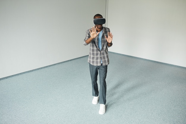 african young man in casual clothing wearing virtual glasses playing in game in empty room