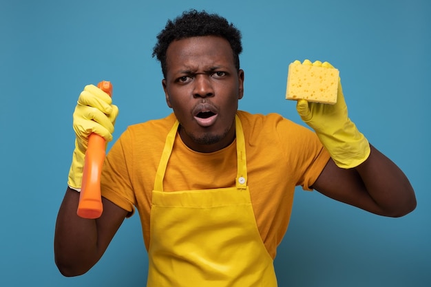 African young man househusband in apron and rubber gloves doing housework