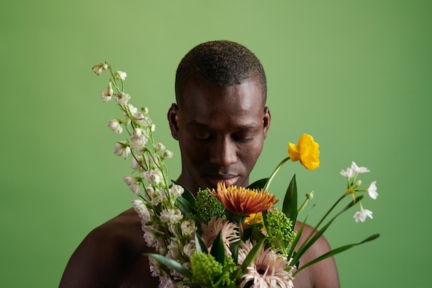 African young man looking at beautiful flowers in his hands standing against the green background