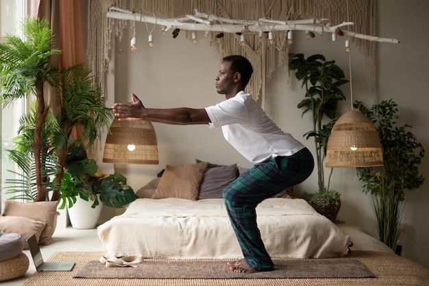 Африканский молодой человек практикует йогу в помещении в ретрите, делая позу стула или Уткатасану дома