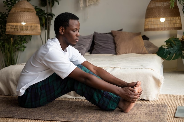 African young man sitting in paschimottanasana or Intense Dorsal Stretch pose seated forward bend posture exercise for hips and spine at home