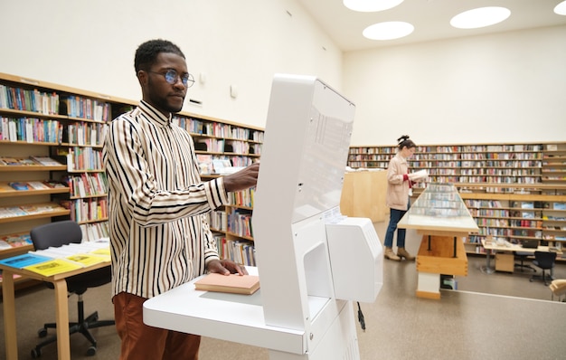 図書館に立って読書のための本を選ぶアフリカの若い男