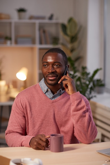 사무실에서 커피를 마시는 테이블에 앉아있는 동안 휴대 전화로 얘기하는 아프리카 젊은 남자