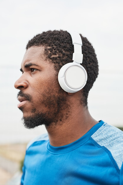 African young sportsman in wireless headphones listening to music outdoors