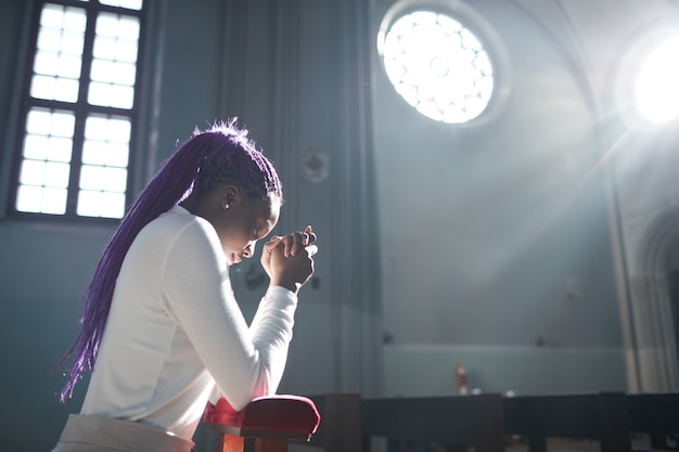 Африканская молодая женщина сидит перед алтарем в церкви и молится