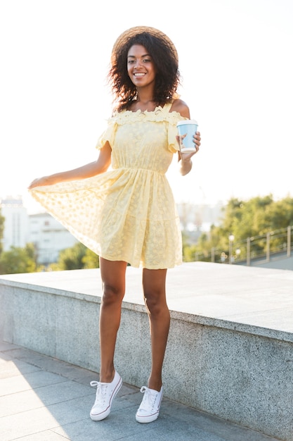 一杯のコーヒーを持って屋外を歩くアフリカの若い女性。