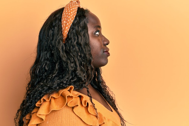 African young woman wearing casual clothes over yellow background looking to side relax profile pose with natural face with confident smile