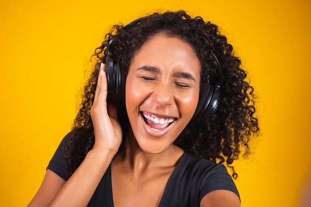 African young woman wearing headphones making a selfie on yellow background.