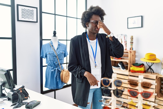 African young woman working as manager at retail boutique smelling something stinky and disgusting intolerable smell holding breath with fingers on nose bad smell