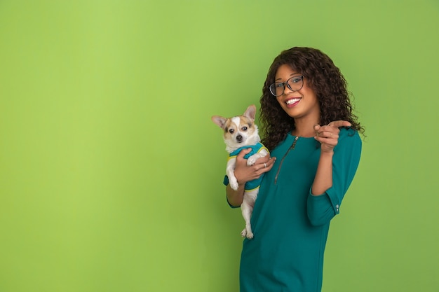 緑のスタジオの背景に小さな犬とアフリカ系アメリカ人の美しい若い女性の肖像画