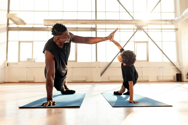 AfricanAmerican boy doing exercises on yoga mat and doing pushups with his dad man training his son