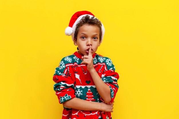 Africanamerican boy in new year's clothes holds his finger near his lips and shows silence