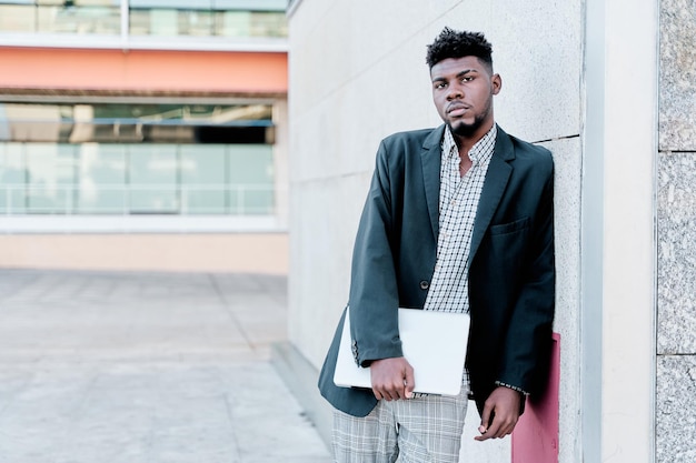 Africanamerican businessman leaning against a wall with a laptop computer copy space for text