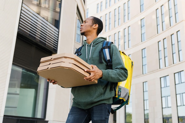 Photo an africanamerican courier with pizza boxes walks through the courtyard of a modern residential complex during delivery