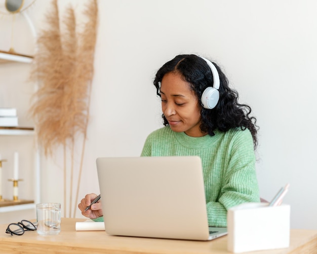 Africanamerican female taking notes while listening to audio podcast in headphones online course