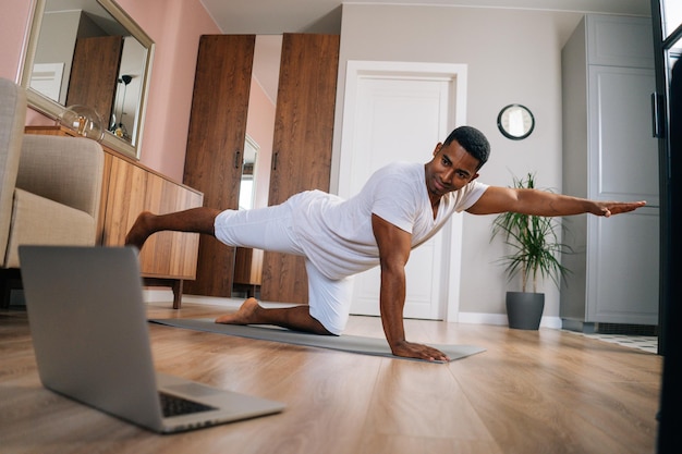 AfricanAmerican fitness instructor explaining exercise in front of laptop during streaming online