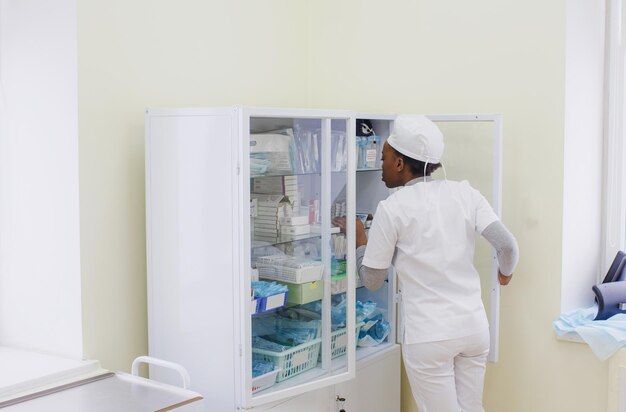 AfricanAmerican girl doctor chooses medicine in a glass cabinet in the treatment room