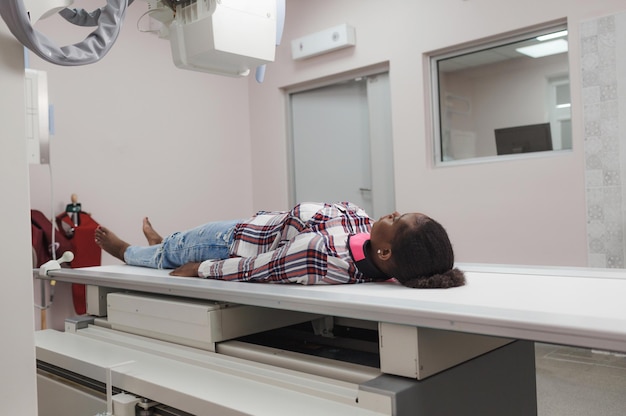 An AfricanAmerican girl is a patient lying on the surface of an apprarat for Xray examination