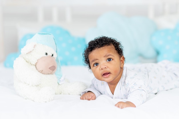 AfricanAmerican little baby in a crib in the bedroom lying on her tummy with a stuffed toy