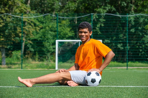 Africanamerican man holding soccer ball while sitting on sports court