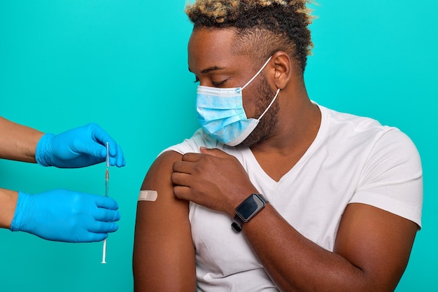 Foto l'uomo afroamericano in una maschera è stato iniettato con un vaccino contro il coronavirus da un medico in guanti blu per l'immunizzazione contro covid19 concetto di vaccinazione e protezione contro covid19