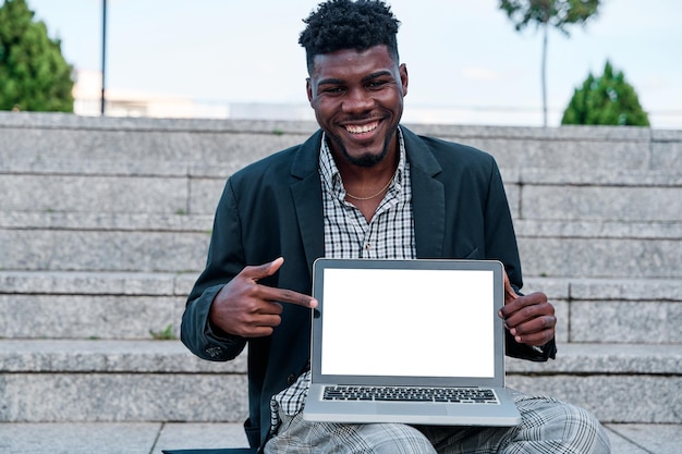 AfricanAmerican man in suit smiling and pointing at blank computer screen mockup