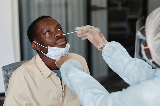 Uomo afroamericano che visita il medico per il tampone nasale per ottenere il test del coronavirus di laboratorio