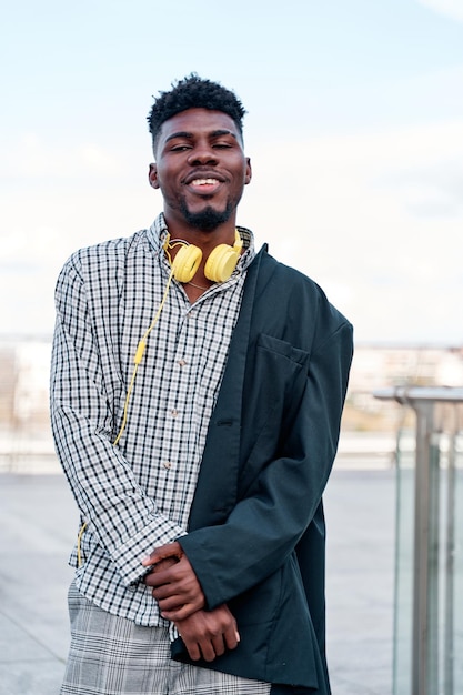 AfricanAmerican man wearing a midlength blazer yellow headphones and plaid shirt