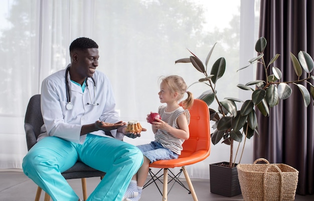 An AfricanAmerican nutritionist tells a little patient about proper and healthy nutrition