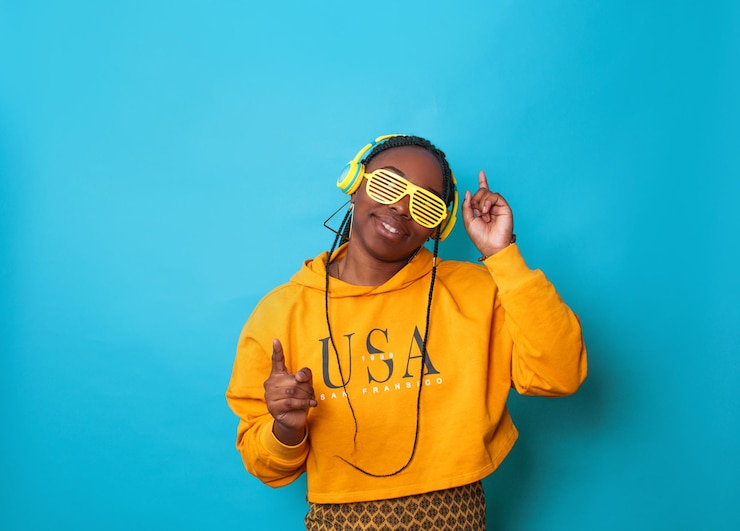 Photo an africanamerican woman listens to music with yellow headphones and stylish glasses on a blue