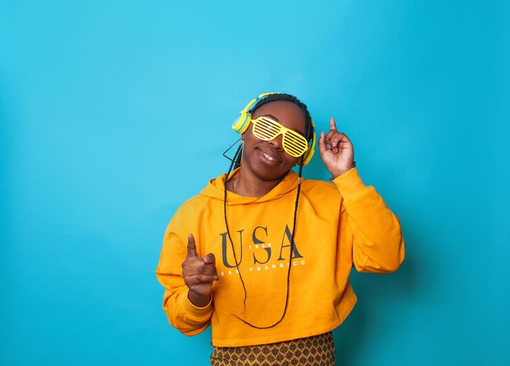 Photo an africanamerican woman listens to music with yellow headphones and stylish glasses on a blue