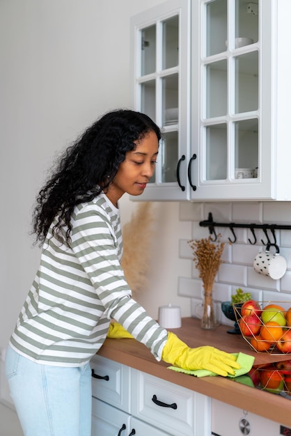 Africanamerican woman occupied with household duties in kitchen wearing yellow rubber gloves