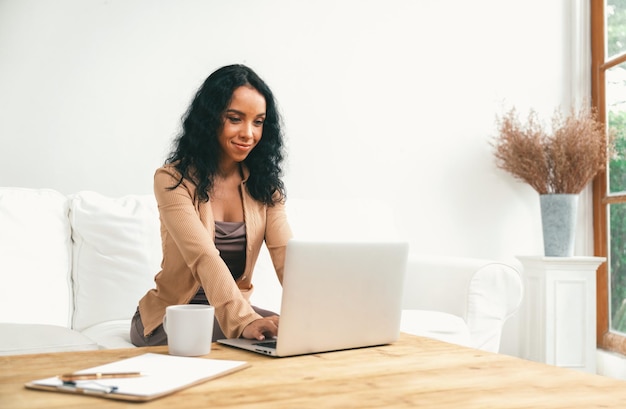 インターネット上の重要な仕事にラップトップ コンピューターを使用するアフリカ系アメリカ人の女性秘書または自宅でオンライン コンテンツの執筆を行う