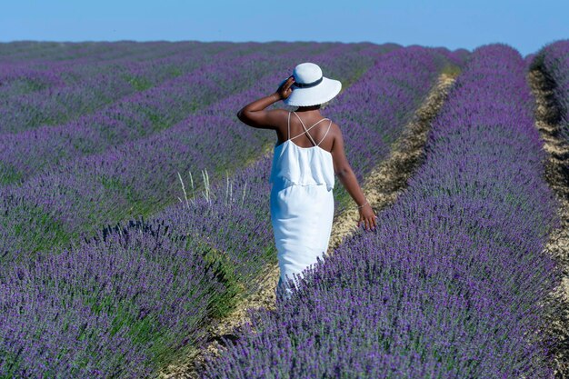 AfricanAmerican woman with white dress and hat strolling between the rows of lavender in bloom