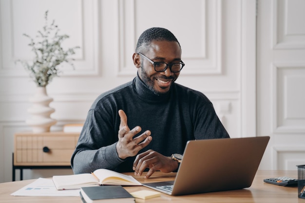 Africanamerican young businessman in glasses having conference online with employes via video call