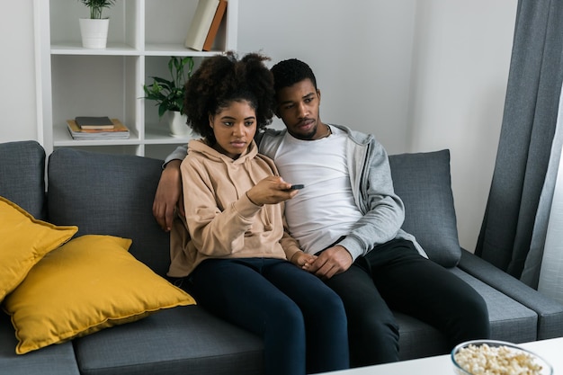 Afrikaans-Amerikaans echtpaar vrouw man kijken naar een film Familie tijdverdrijf en vrije tijd kijken naar televisie rust Ontspannen man en vrouw kijken samen naar tv-series zitten thuis op de bank en genieten van het eten van popcorn